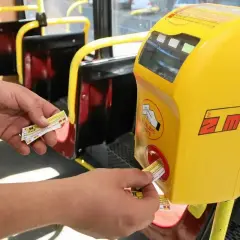 Ręka wsuwa bilet 20 minutowy Warszawa do żółtego kasownika w autobusie.