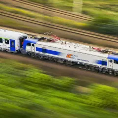 Pociąg PKP Intercity pędzi przez zielone krajobrazy. Dowiedz się, jak kupić bilet rodzinny PKP przez internet, by podróżować z bliskimi.
