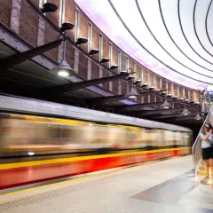 Nowoczesna stacja metra, do której jeździ metro. Pociąg mija peron, a ludzie schodzą po schodach.