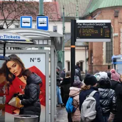 Kraków: ludzie czekają na przystanku, kupują bilety na komunikację miejską. W tle tramwaj i kościół.