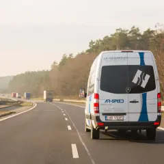 Biały bus AR-SPEED jedzie autostradą, realizując przewozy międzynarodowe Polska-Holandia. To szybki bus od drzwi do drzwi.