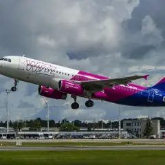 Samolot Wizz Air z różowymi silnikami startuje, a na lotnisku trwa przebookowanie pasażerów.
