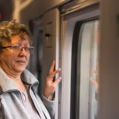 Starsza pani w okularach, podróżująca pociągiem PKP Intercity, cieszy się z 70 lat darmowych przejazdów.