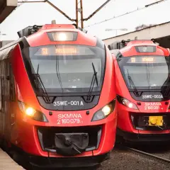 Dwa czerwone pociągi SKM, szybka kolej miejska w Warszawie, stoją na peronie. Jeden z nich kieruje się do Pruszkowa.