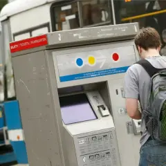 Młody mężczyzna z plecakiem kupuje bilet czasowy Wrocław na automacie przy niebieskim tramwaju.