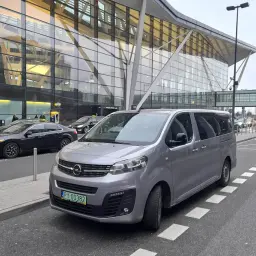 Szary van czeka na pasażerów przed nowoczesnym terminalem lotniska. Może to być transport z Koszalina do Gdańska.