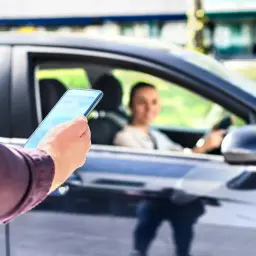 Mężczyzna z telefonem czeka na pasażera. To carpooling co to? Wspólne dojazdy do pracy lub na uczelnię.