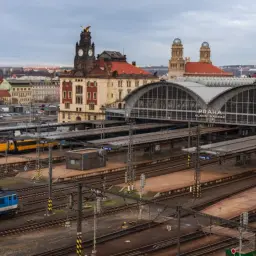 Pociąg do Czech czeka na dworcu Praha Hlavní Nádraží. Widać żółty pociąg RegioJet i niebieską lokomotywę.