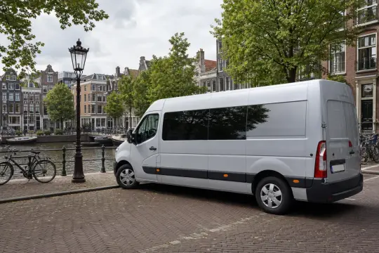 Biały bus do Holandii zaparkowany przy kanale w Amsterdamie, obok rowerów i zabytkowych kamienic.