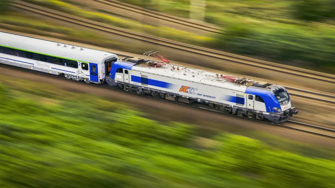 Pociąg PKP Intercity pędzi przez zielone krajobrazy. Dowiedz się, jak kupić bilet rodzinny PKP przez internet, by podróżować z bliskimi.