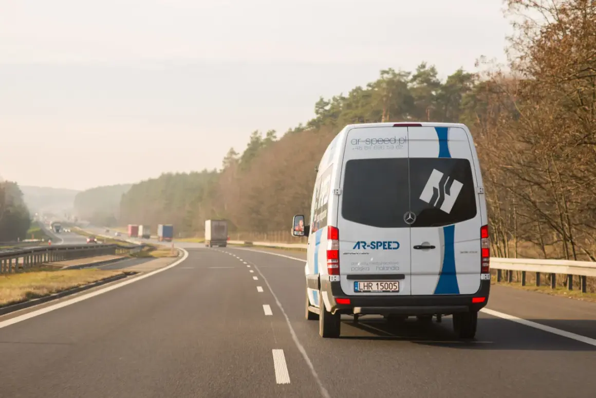 Biały bus AR-SPEED jedzie autostradą, realizując przewozy międzynarodowe Polska-Holandia. To szybki bus od drzwi do drzwi.