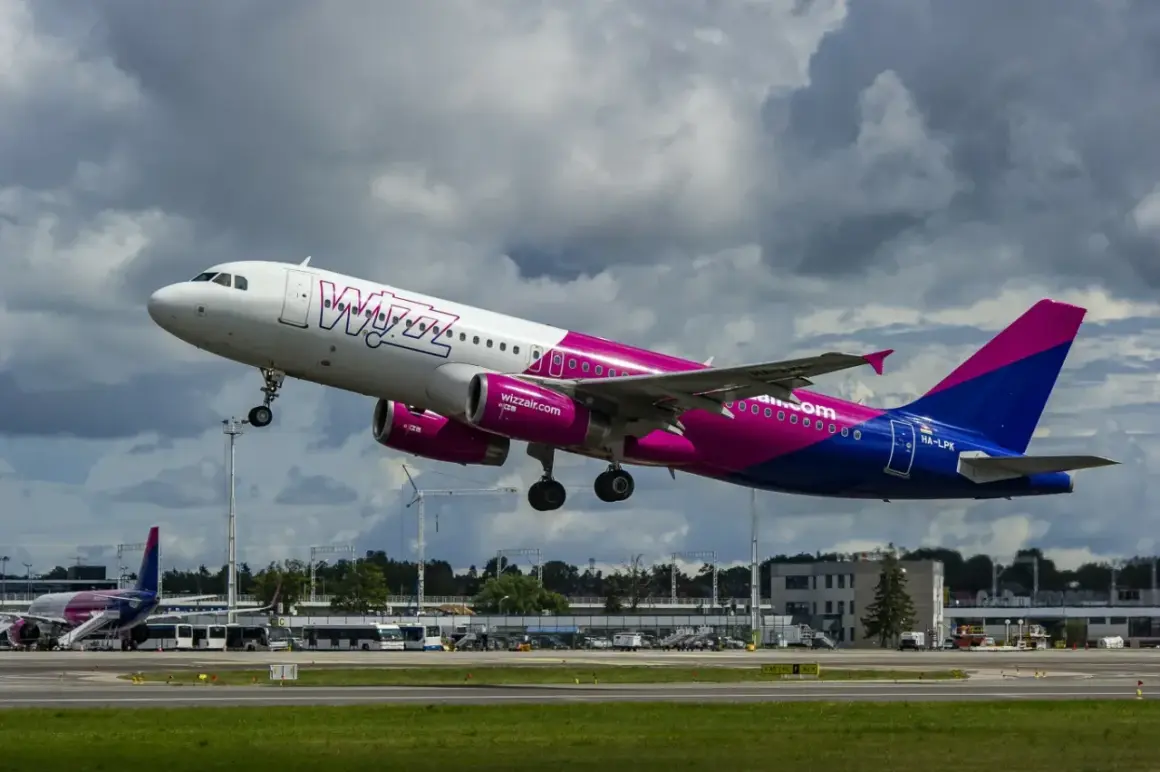 Samolot Wizz Air z różowymi silnikami startuje, a na lotnisku trwa przebookowanie pasażerów.