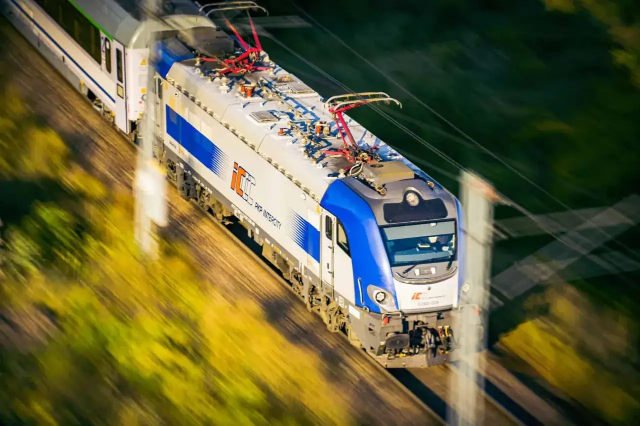 Pędzący pociąg PKP Intercity z niebiesko-białą lokomotywą. W tle rozmyty krajobraz. 70 lat darmowe przejazdy PKP Intercity.