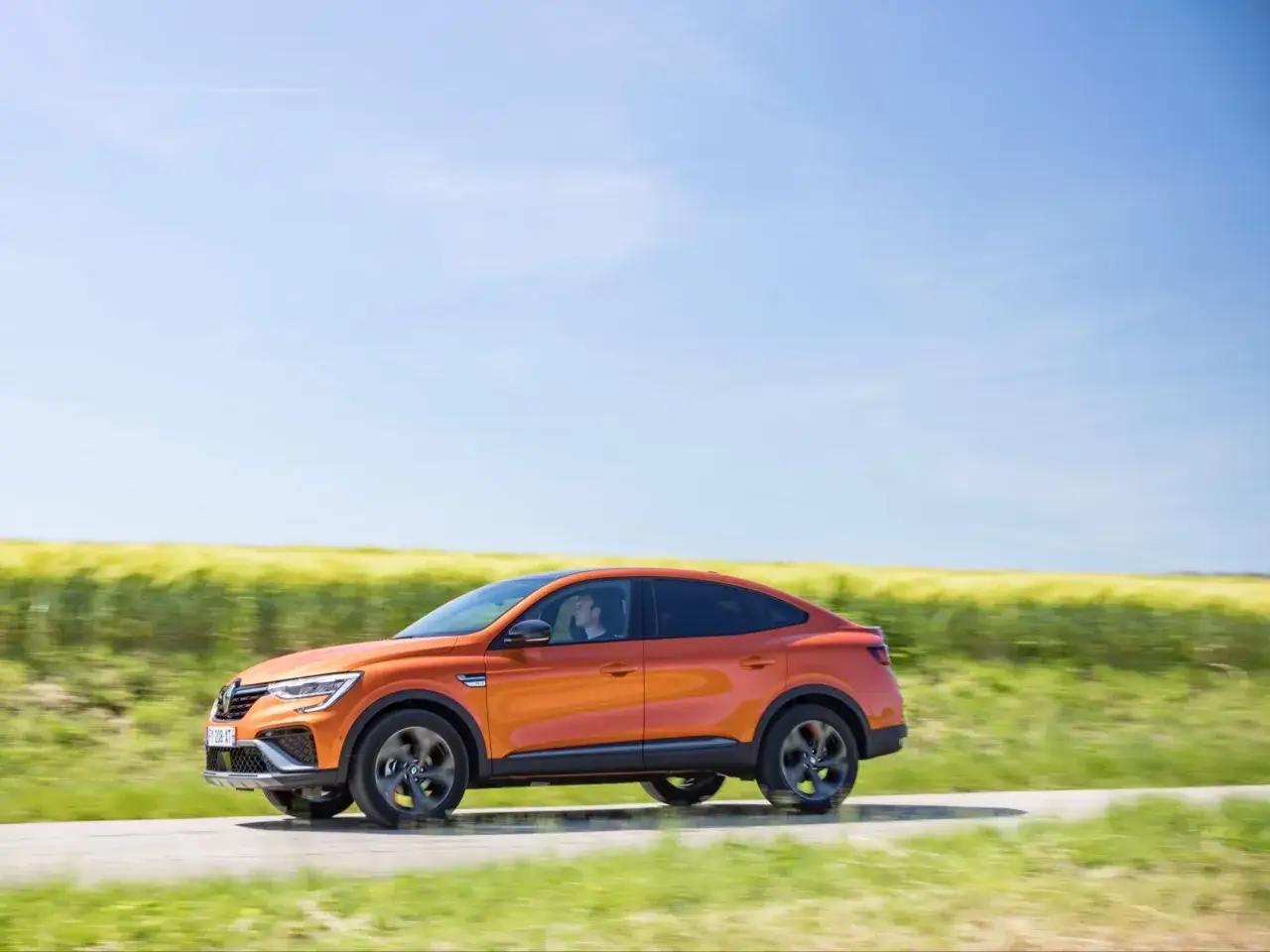 Pomarańczowy SUV jedzie drogą przez pole. Kierowca w samochodzie, który może być użyty do podróży BlaBlaCar, cieszy się jazdą.