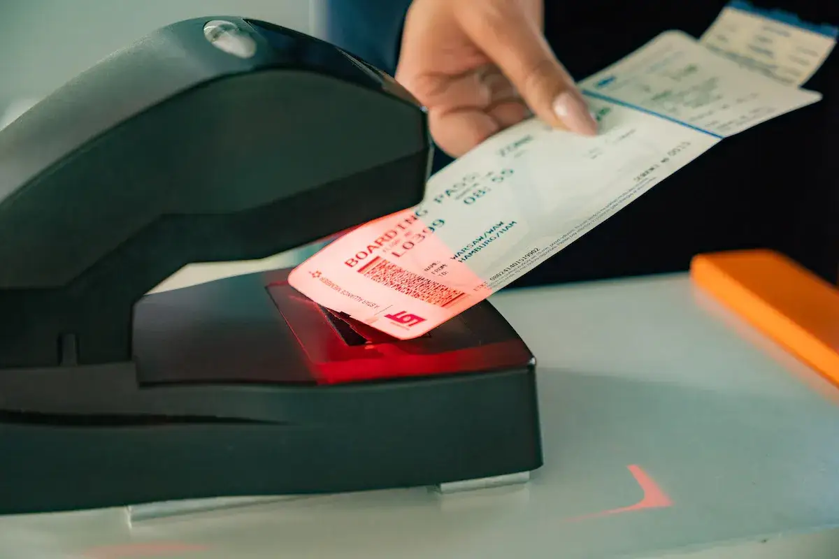 Ręka skanuje kartę pokładową LOT. Czerwony promień skanera oświetla kod QR, przygotowując do przebookowania.