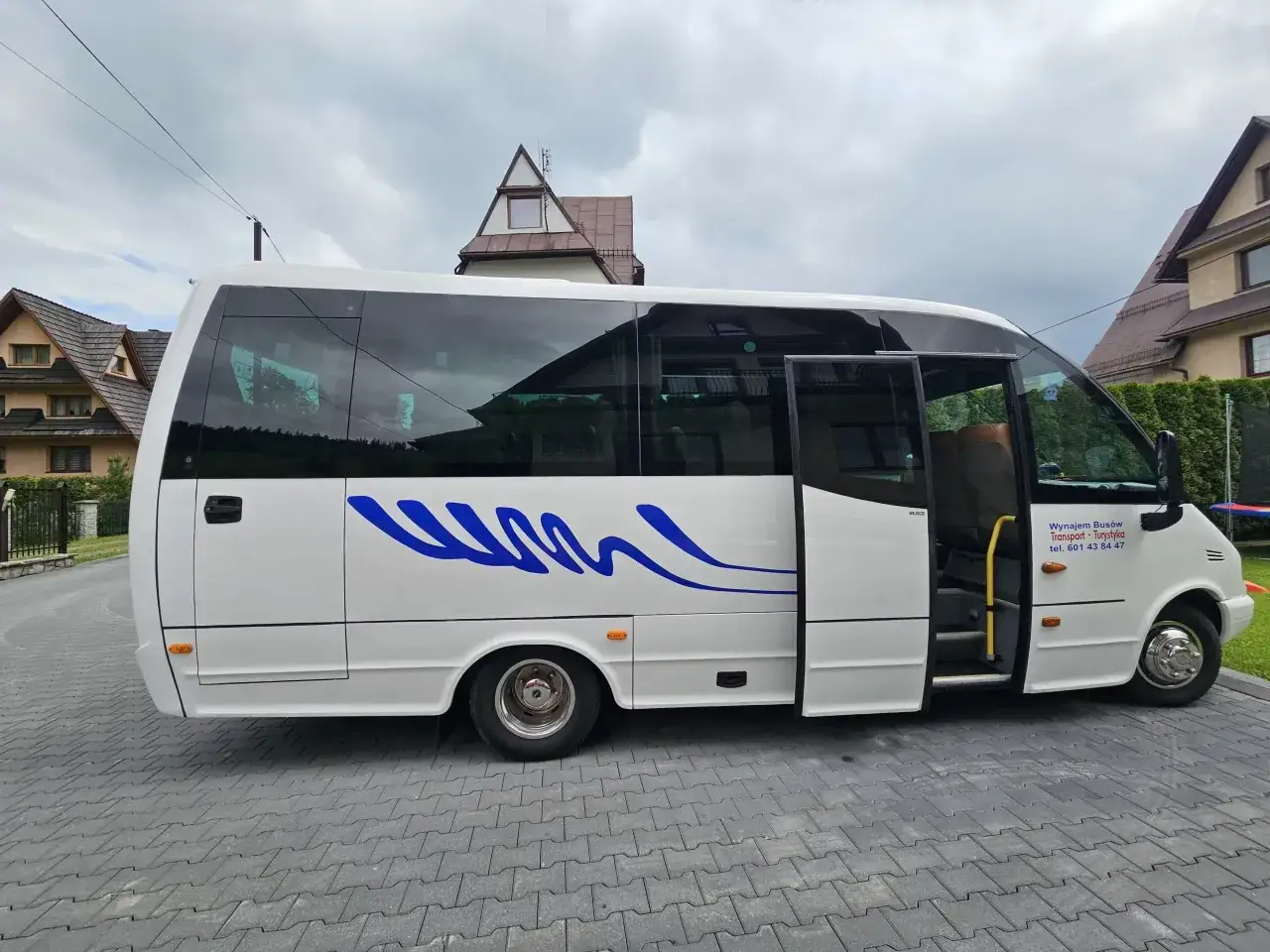 Biały bus z niebieskim wzorem, gotowy na wycieczkę. Szukasz transportu do Kościeliska? Sprawdź cenę wynajmu busów w Zakopanem!