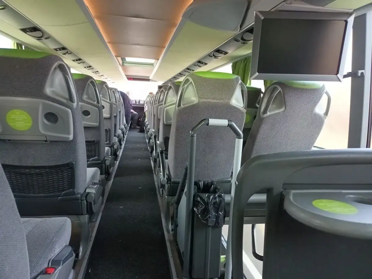 Wnętrze Flixbus autobus, rzędy szarych siedzeń z zielonymi zagłówkami, ekranik nad siedzeniami.