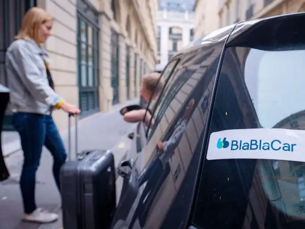 Kobieta z walizką wsiada do samochodu z logo BlaBlaCar. Tak działa wspólne podróżowanie.