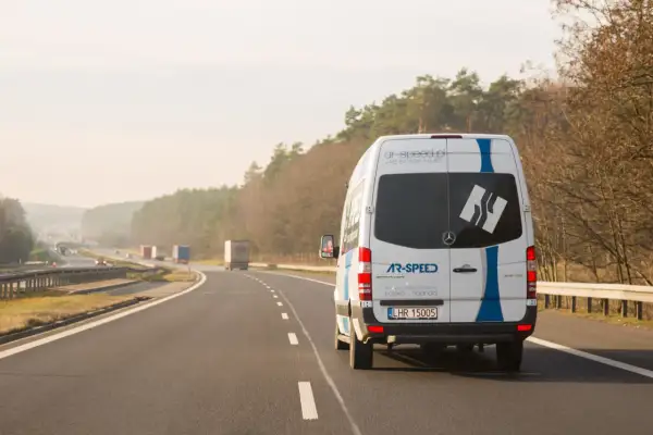 Biały bus AR-SPEED jedzie autostradą, realizując przewozy międzynarodowe Polska-Holandia. To szybki bus od drzwi do drzwi.
