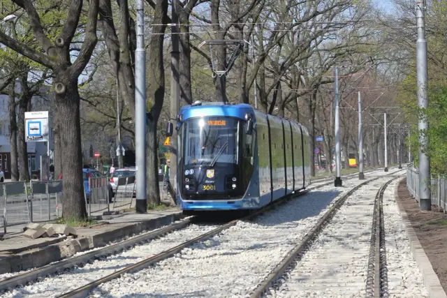 Nowoczesny tramwaj MPK Wrocław z numerem 3001 jedzie po torach wśród drzew. Aplikacja MPK Wrocław ułatwia podróżowanie.
